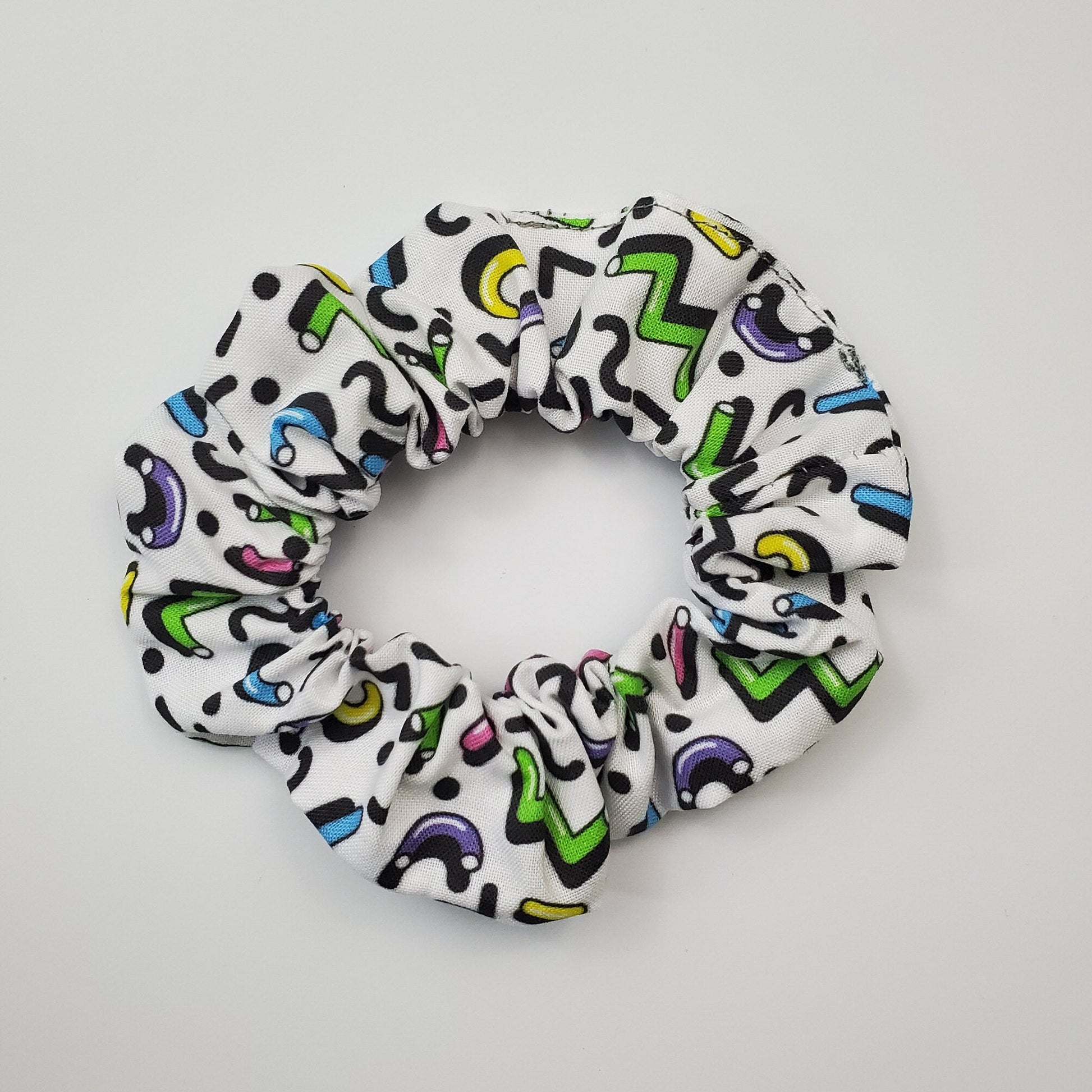 White scrunchie with brightly colored squiggle design - 90s inspired. Some purple, some green, yellow, hot pink, and black squiggles in macaroni shapes, zig zags, etc.