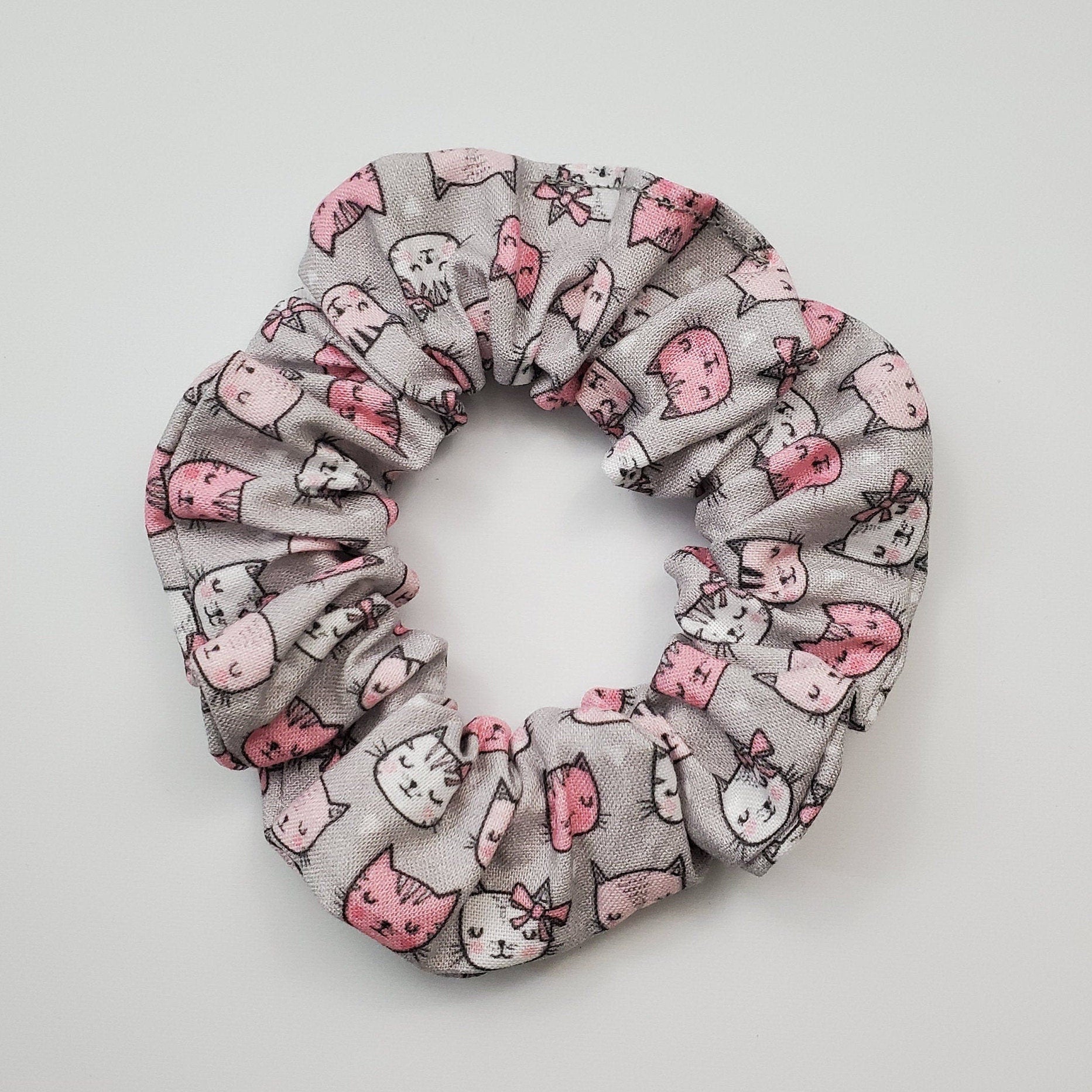 Grey and pink cats scrunchie - a grey background fabric with white and pink cartoon cat heads.
