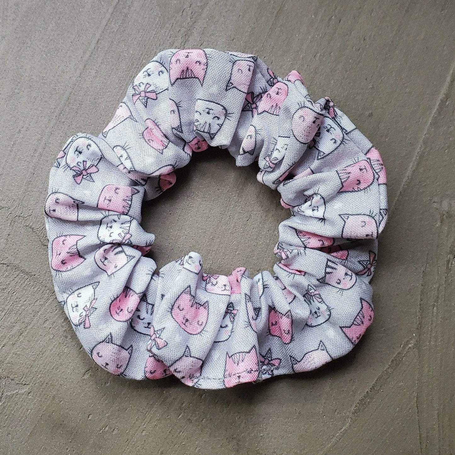 Grey and Pink cats Biodegradable Scrunchie in natural sunlight on a concrete background.