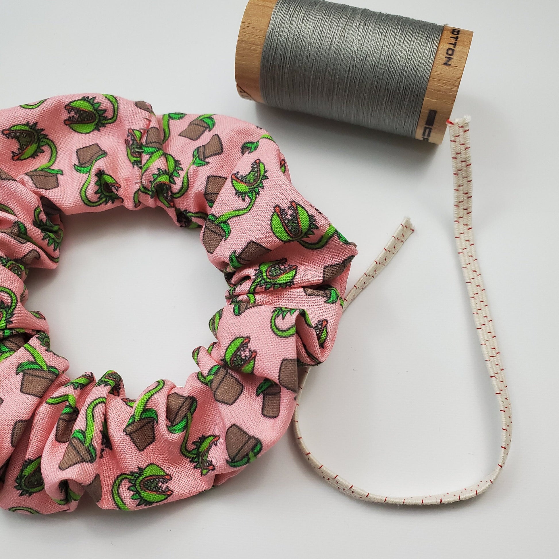 Scrunchie shown next to a wooden spool of grey thread, and a piece of the biodegradable elastic.