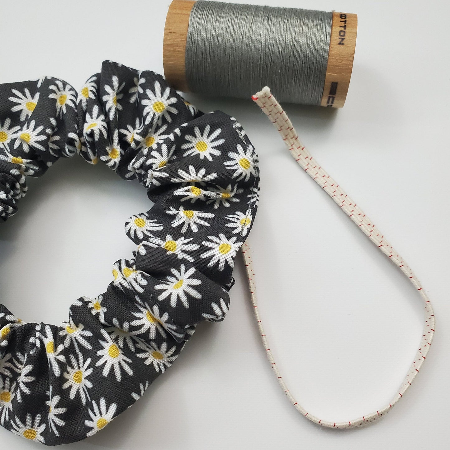 Scrunchie shown next to a wooden spool of grey thread, and a piece of the biodegradable elastic.