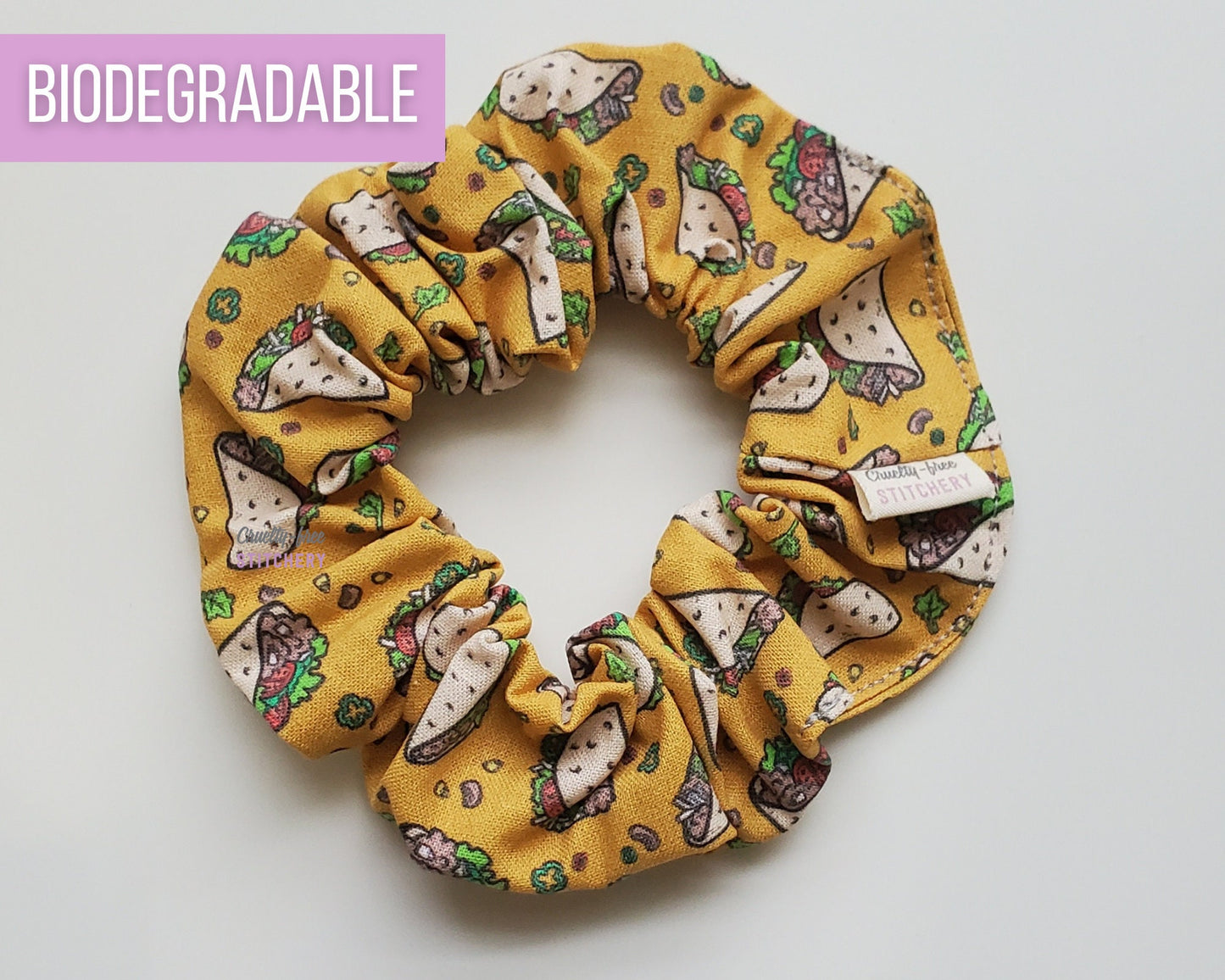 Mustard yellow scrunchie with cartoonish printed tacos. Tacos and fillings are scattered around.