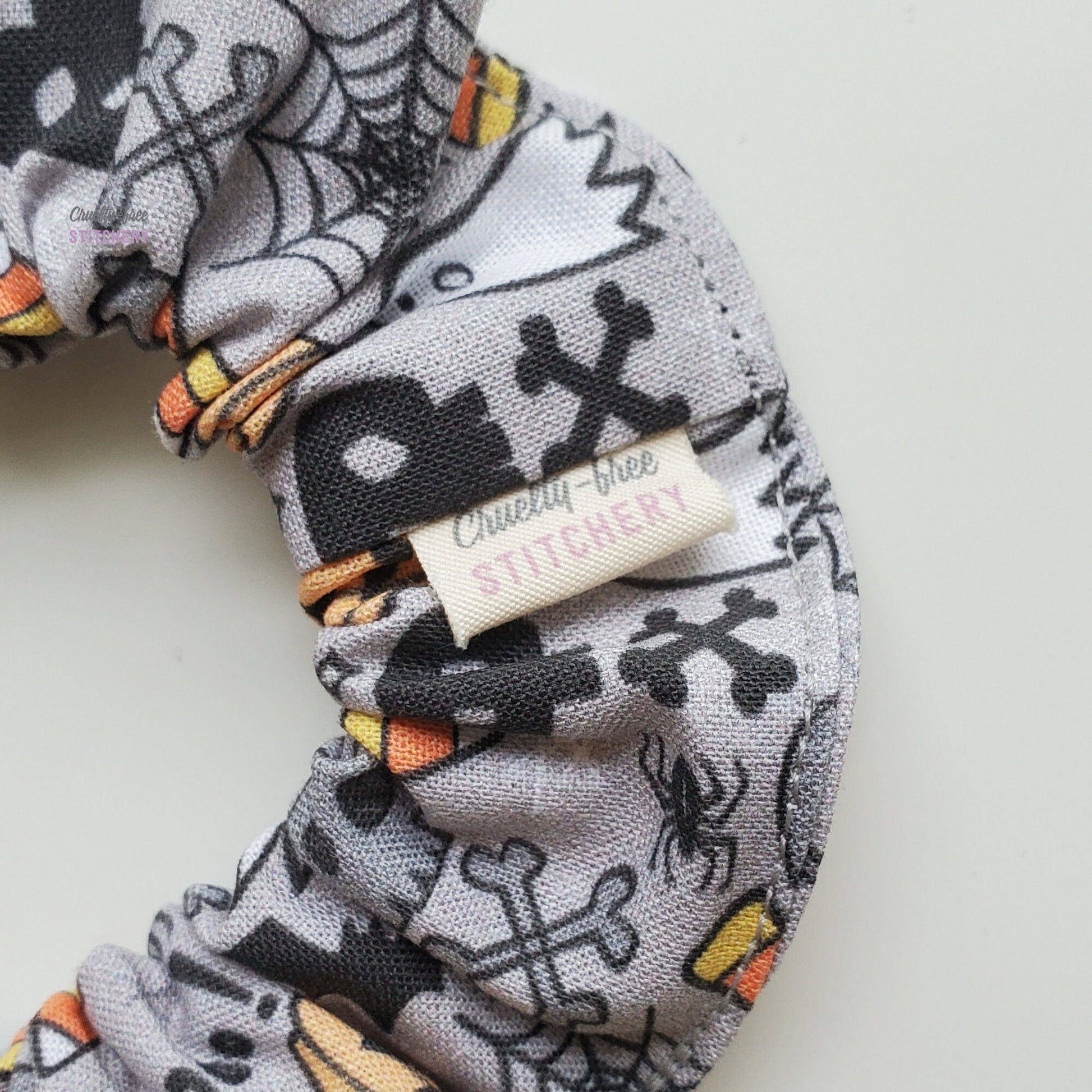 Close-up of the Halloween doodle scrunchie with a small white tag with the Cruelty-Free Stitchery logo.