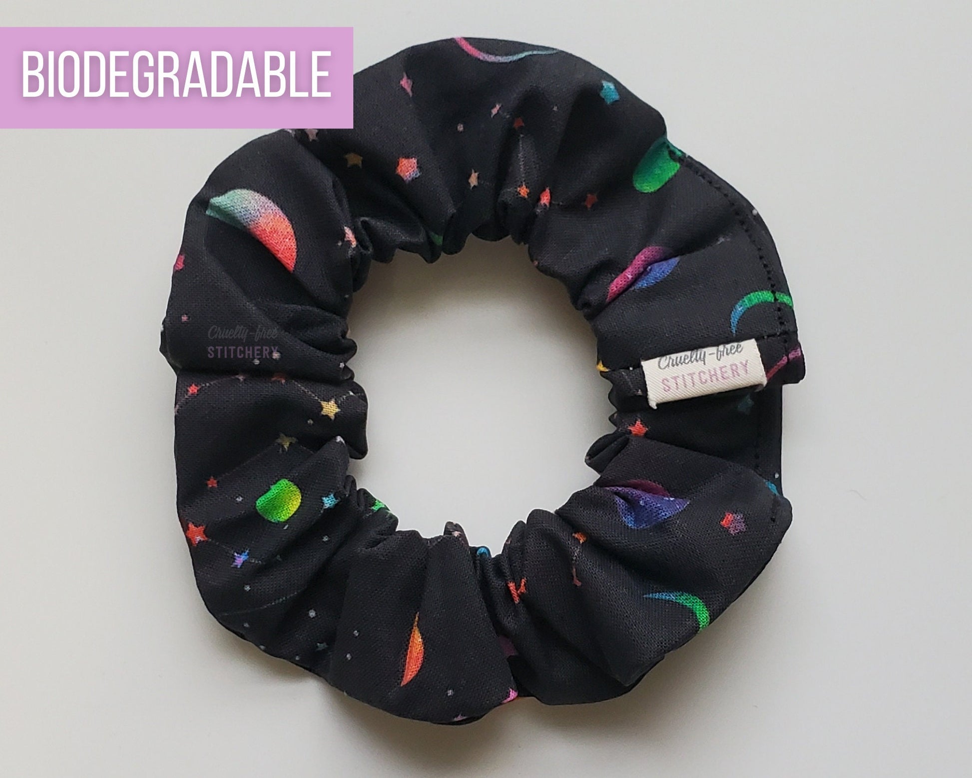 A black scrunchie with rainbow ombre colored stars and moons.