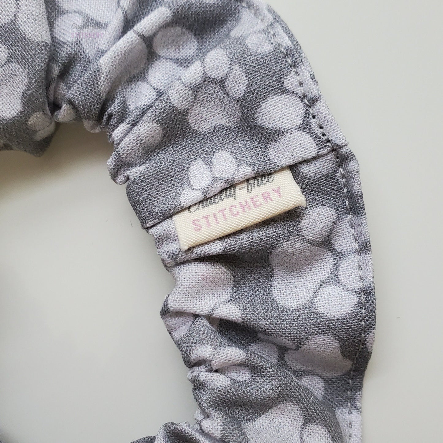 Close-up of the gray paw print scrunchie with a small white tag with the Cruelty-Free Stitchery logo.