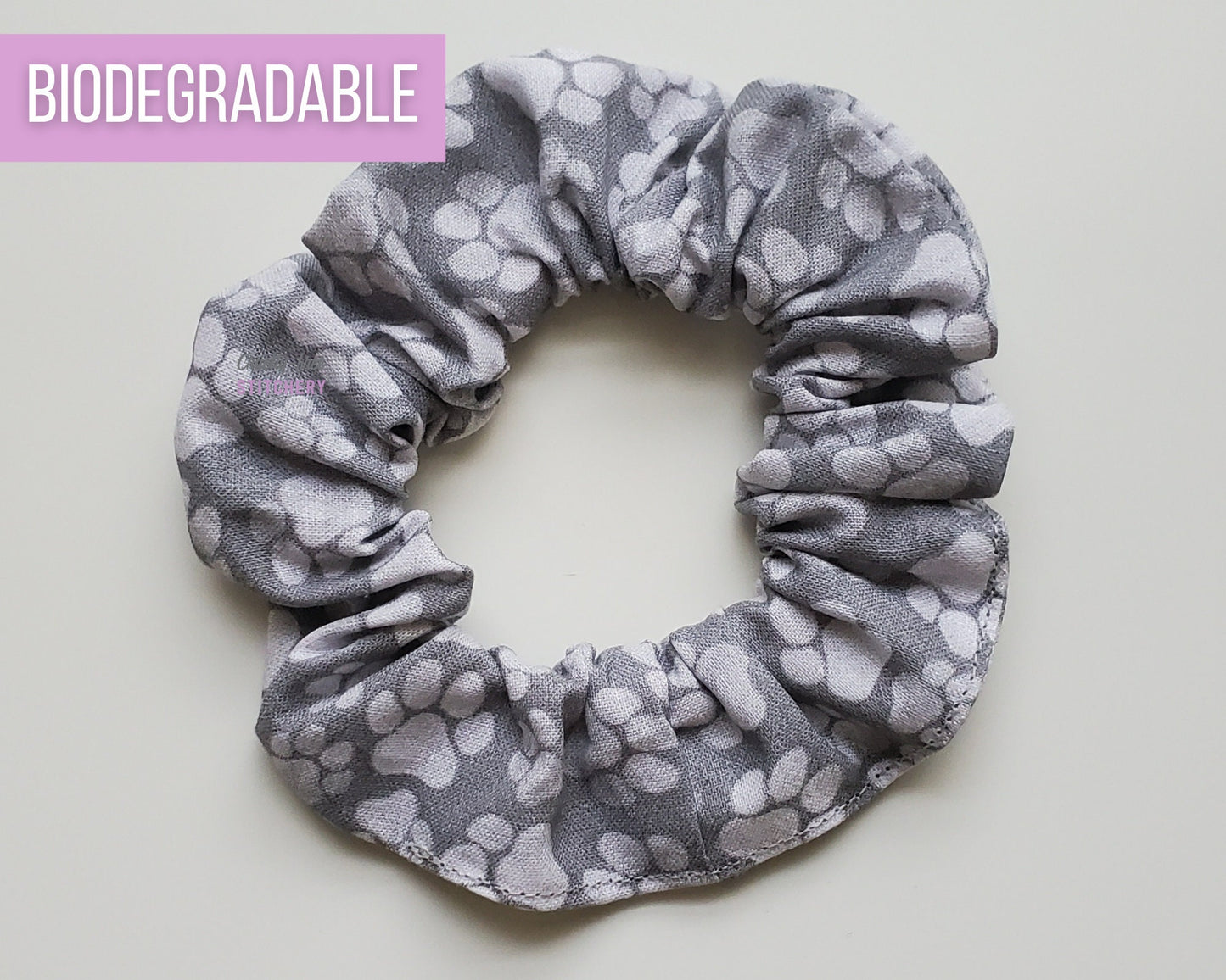 Grey paw print scrunchie. A medium gray fabric with lighter gray paw prints in various sizes.