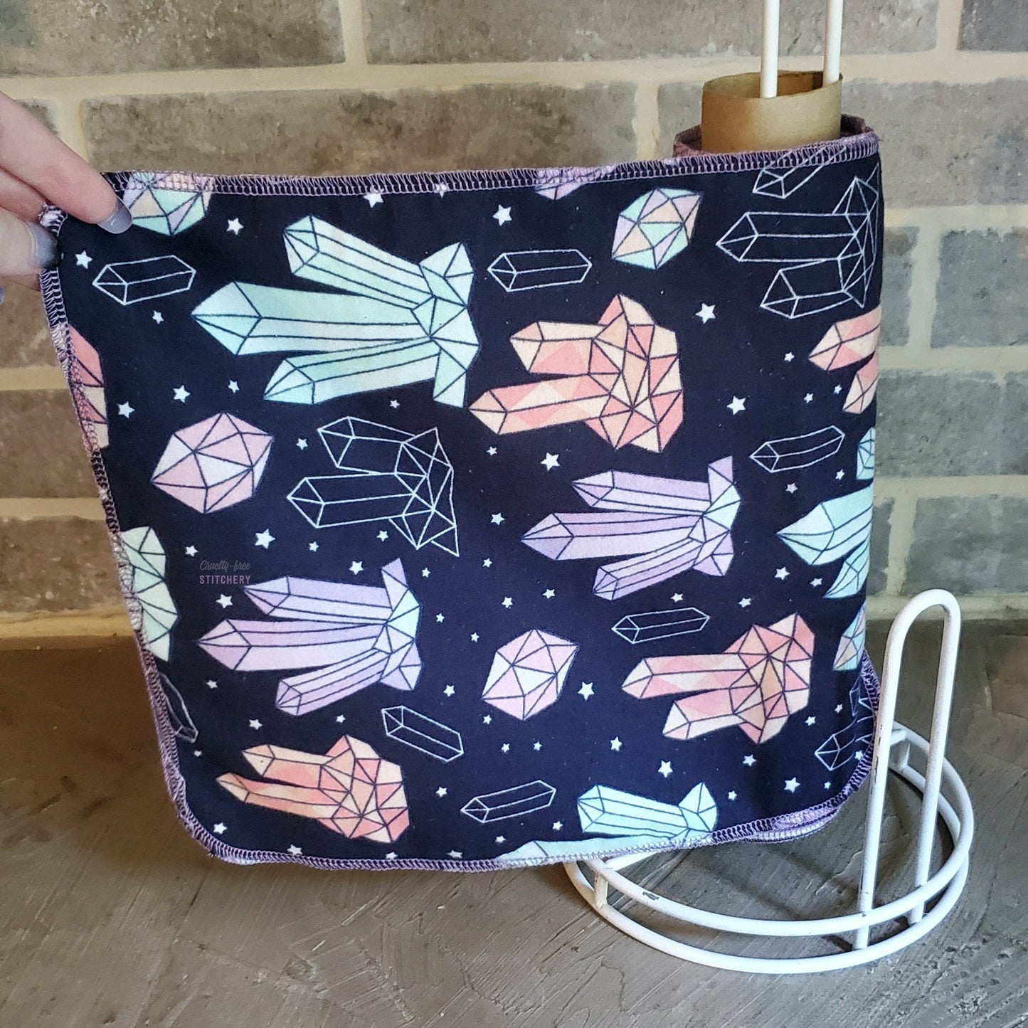 A roll of crystal print NonPaper Towels. The fabric is dark navy blue with drawn pink, purple, and light blue crystals and tiny white stars.