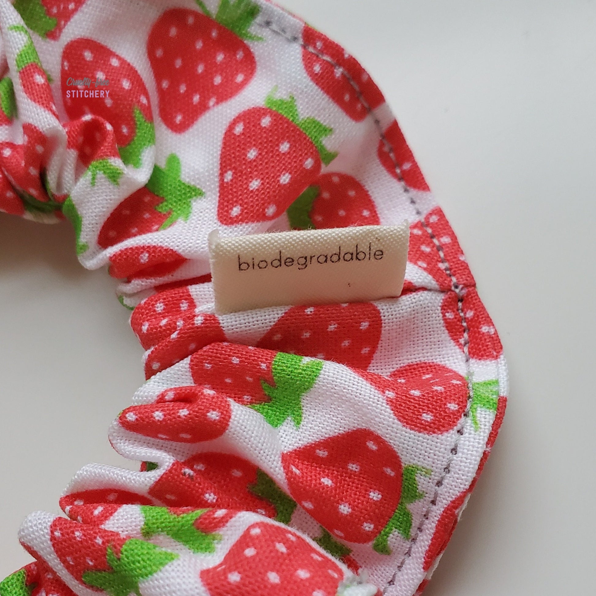 Close-up image of the scrunchie with the back side of the small tag, with the word "biodegradable" printed on it.