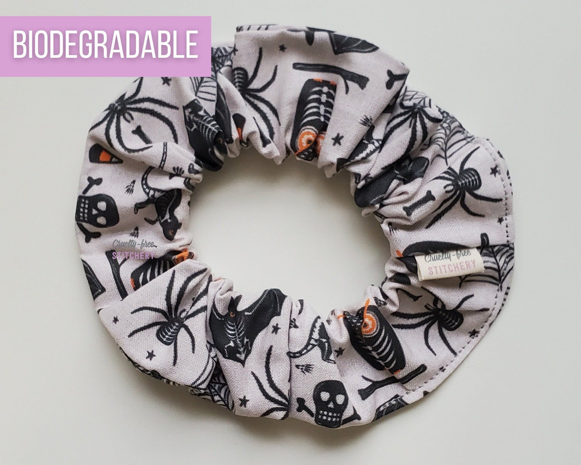 Halloween scrunchie - a light grey with various spooky motifs like spiders, owls, skulls, and bats. The owls have orange eyes.