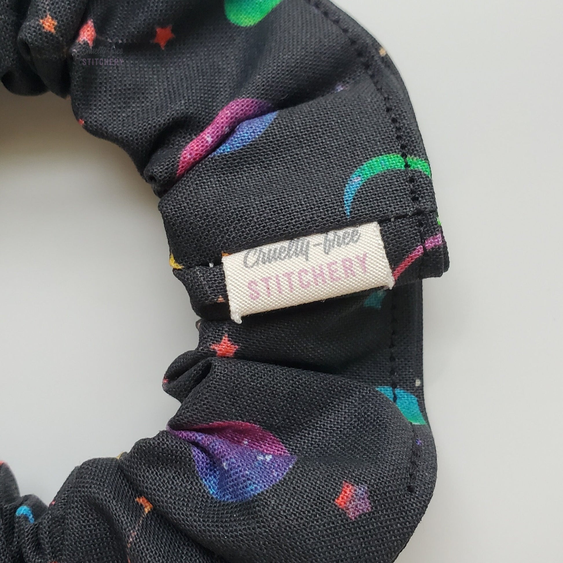 Close-up of the black with rainbow stars scrunchie with a small white tag with the Cruelty-Free Stitchery logo.
