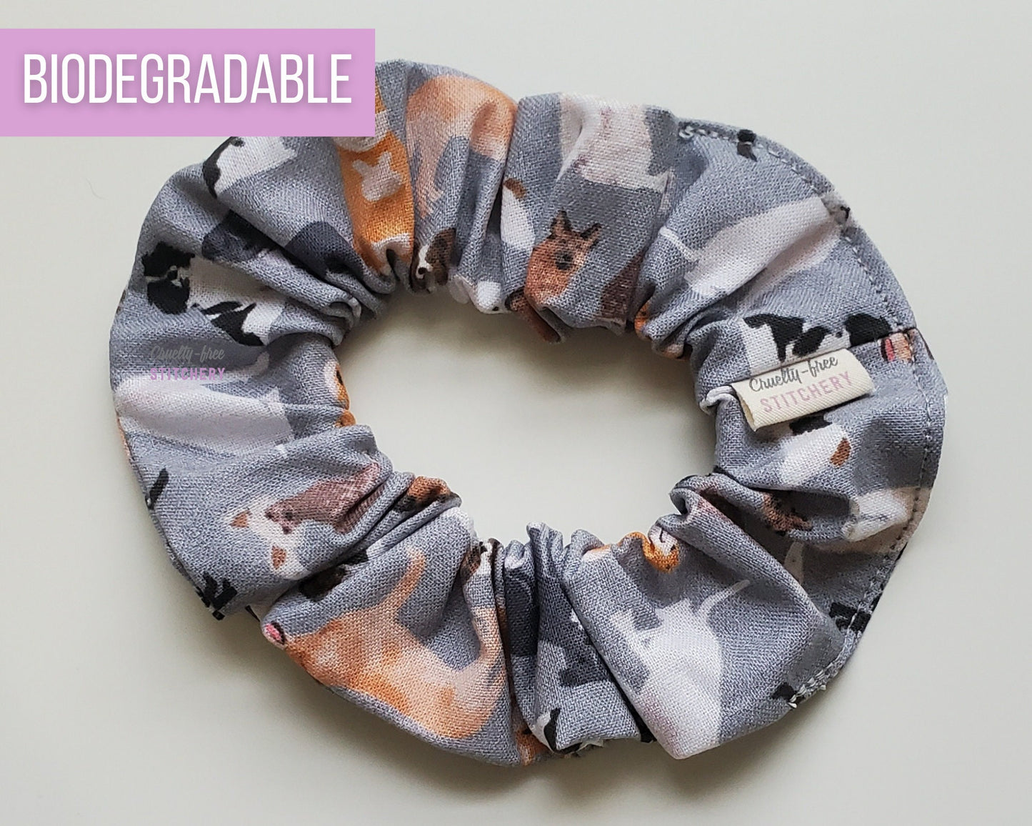 Grey with dogs print scrunchie. A light grey fabric with various printed dogs like German Shepherds, Labs, Poodles, Yorkies, and many more.