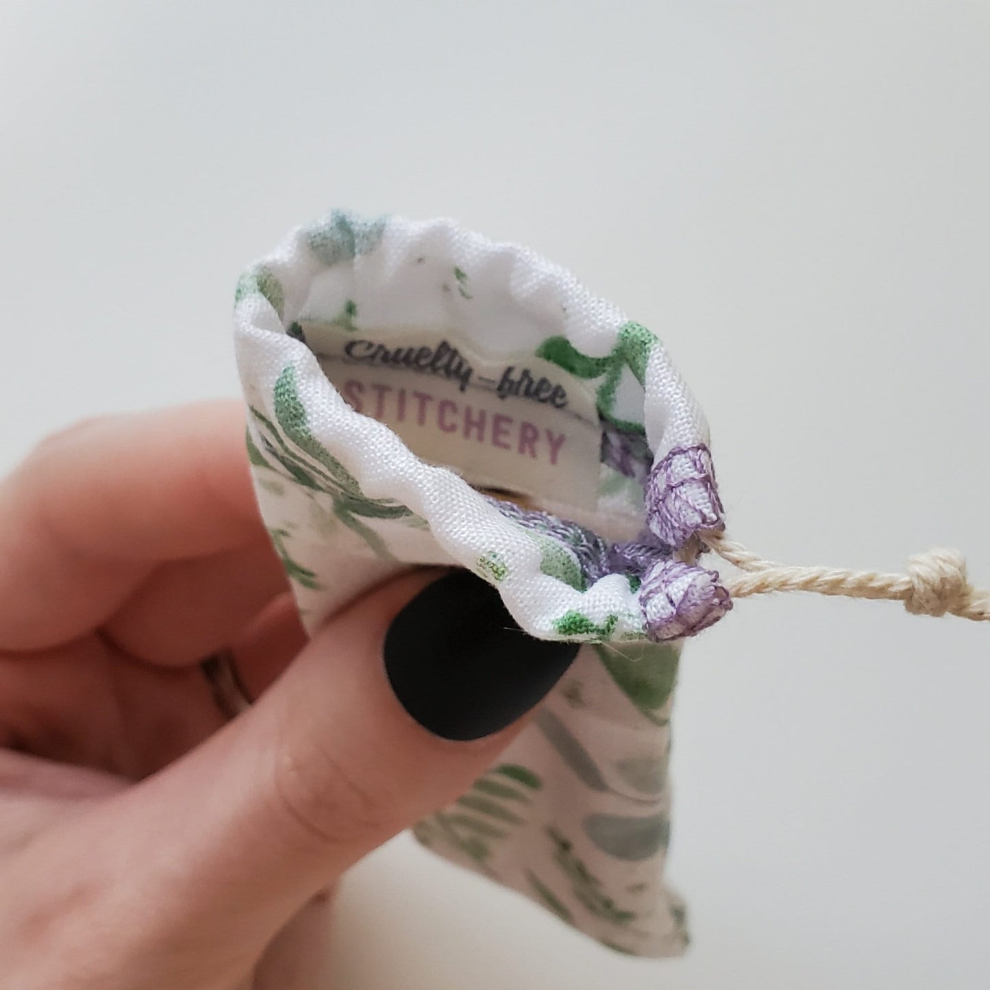 A reusable spork pouch, viewed from the top down. Inside the pouch is a tag with the Cruelty-Free Stitchery logo. The pouch is in someone's hand, the width is about half as wide as the thumb is long.