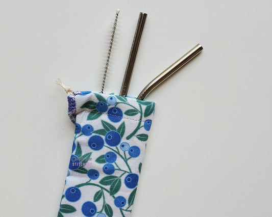 Reusable straw pouch with stainless steel straws sticking out the top. The fabric of the pouch is white with blueberry vines printed on, and it has a drawstring closure.