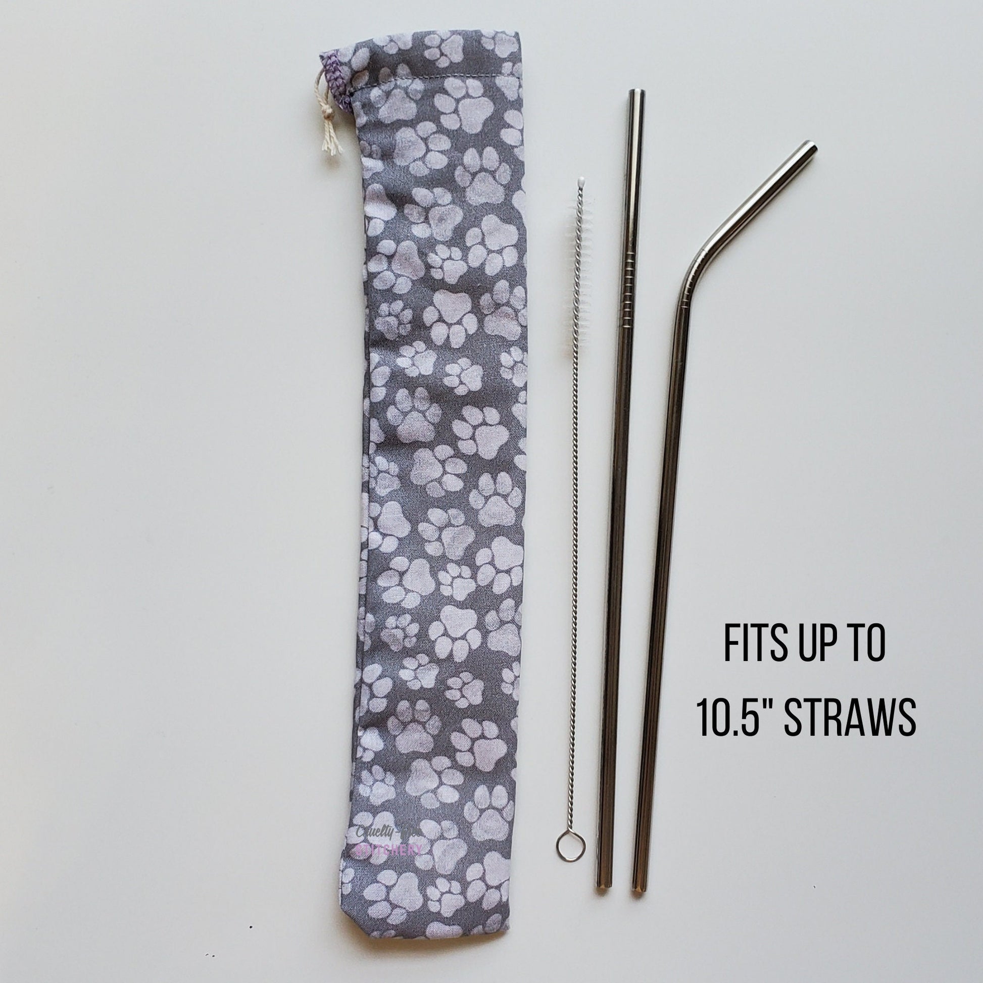 Reusable straw pouch in the same paw print fabric laying vertically next to a straw cleaner brush, a straight stainless steel straw, and a bent stainless steel straw. Text reads &quot;fits up to 10.5 inch straws&quot;