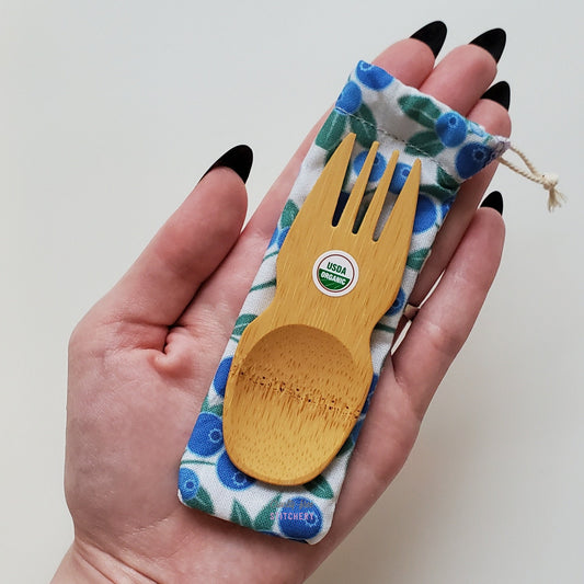 Reusable bamboo spork with pouch. Blueberry print fabric pouch with bamboo spork on top, laid on a hand for size reference.