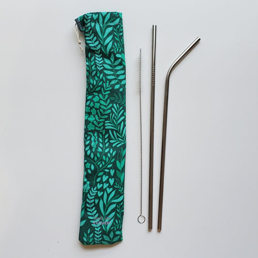 Reusable straw pouch in the same green with leaves print laying vertically next to a straw cleaner brush, a straight stainless steel straw, and a bent stainless steel straw.