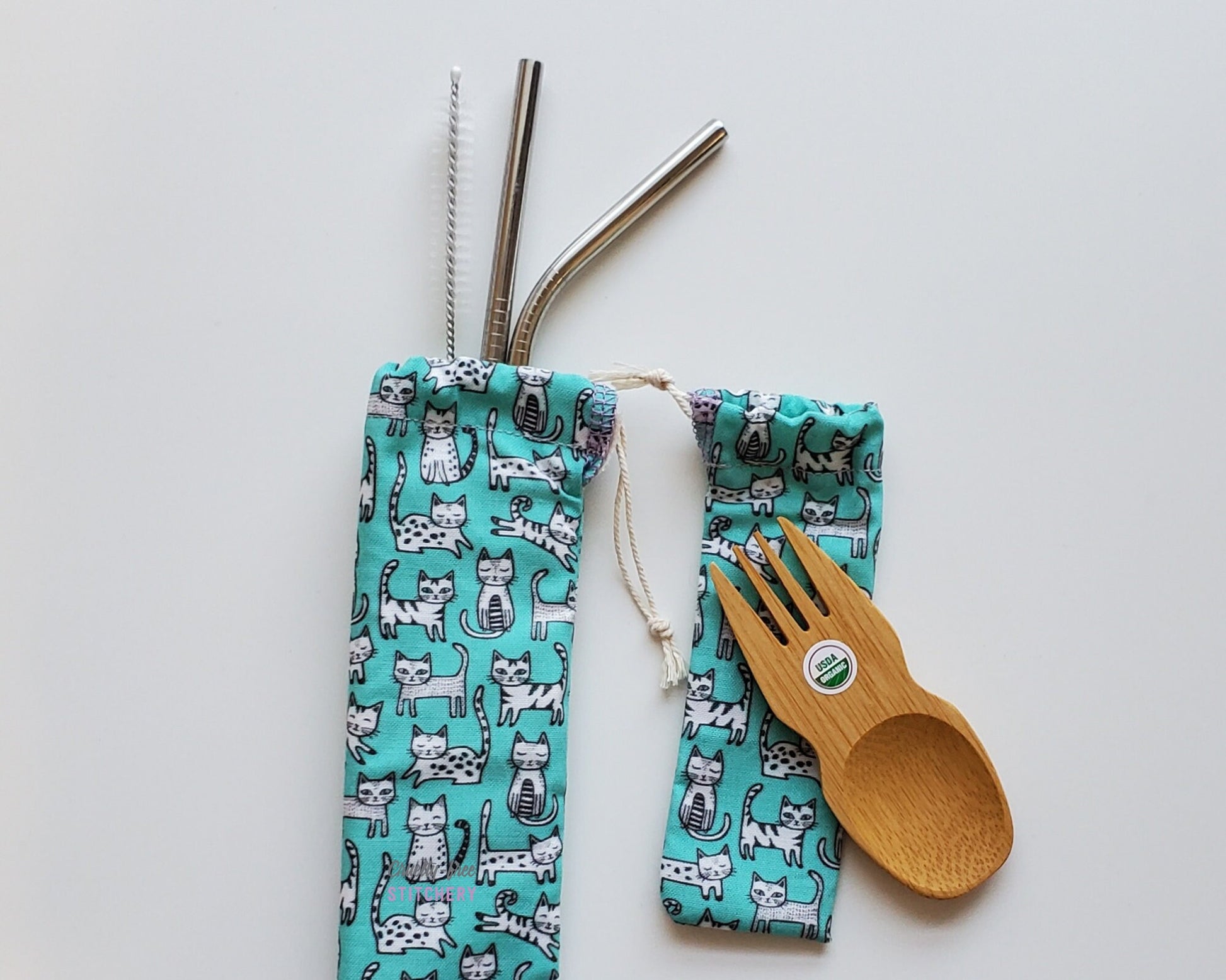 Reusable bamboo spork and stainless steel straw pouch set. The pouches are both light blue with tiny black and white cartoon cats in various styles and positions like sitting up, laying down, jumping, etc.