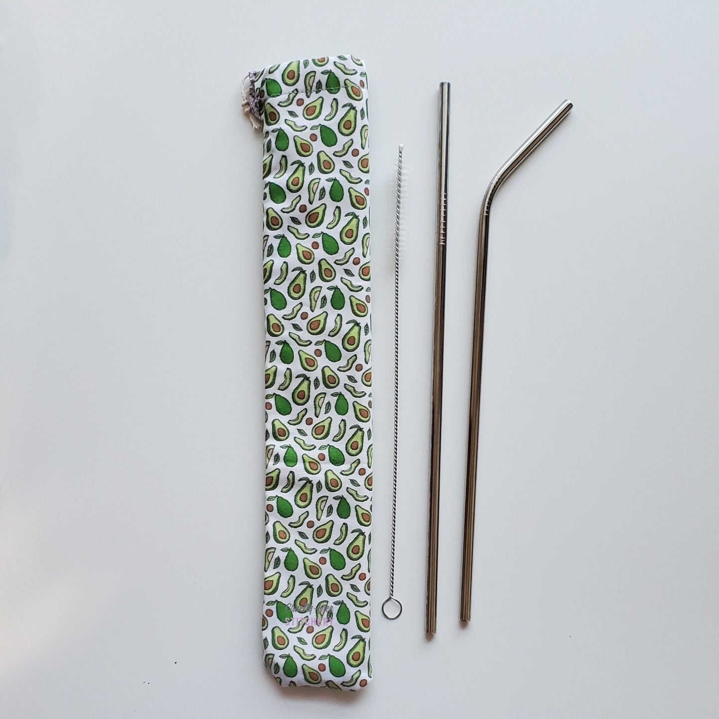 Reusable straw pouch in the same avocado print laying vertically next to a straw cleaner brush, a straight stainless steel straw, and a bent stainless steel straw.