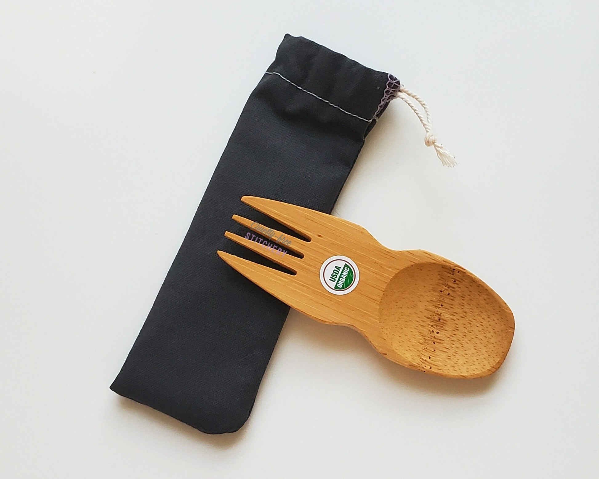 Solid black reusable spork pouch. The pouch is sitting diagonally with the spork partially on top pointing the other way. The fork end of the spork is pointing to the left.