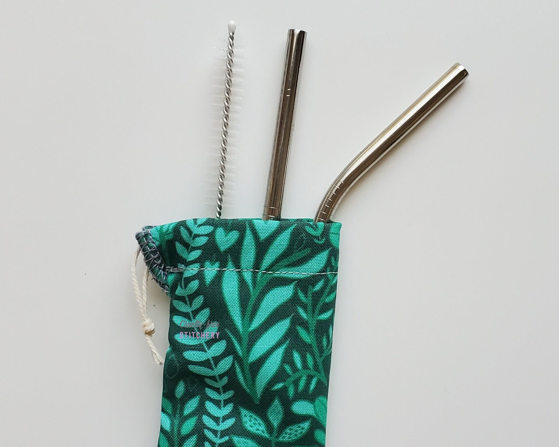 Reusable straw pouch with stainless steel straws sticking out the top. The fabric of the pouch is dark green with lighter green leaves and vines, and it has a drawstring closure.