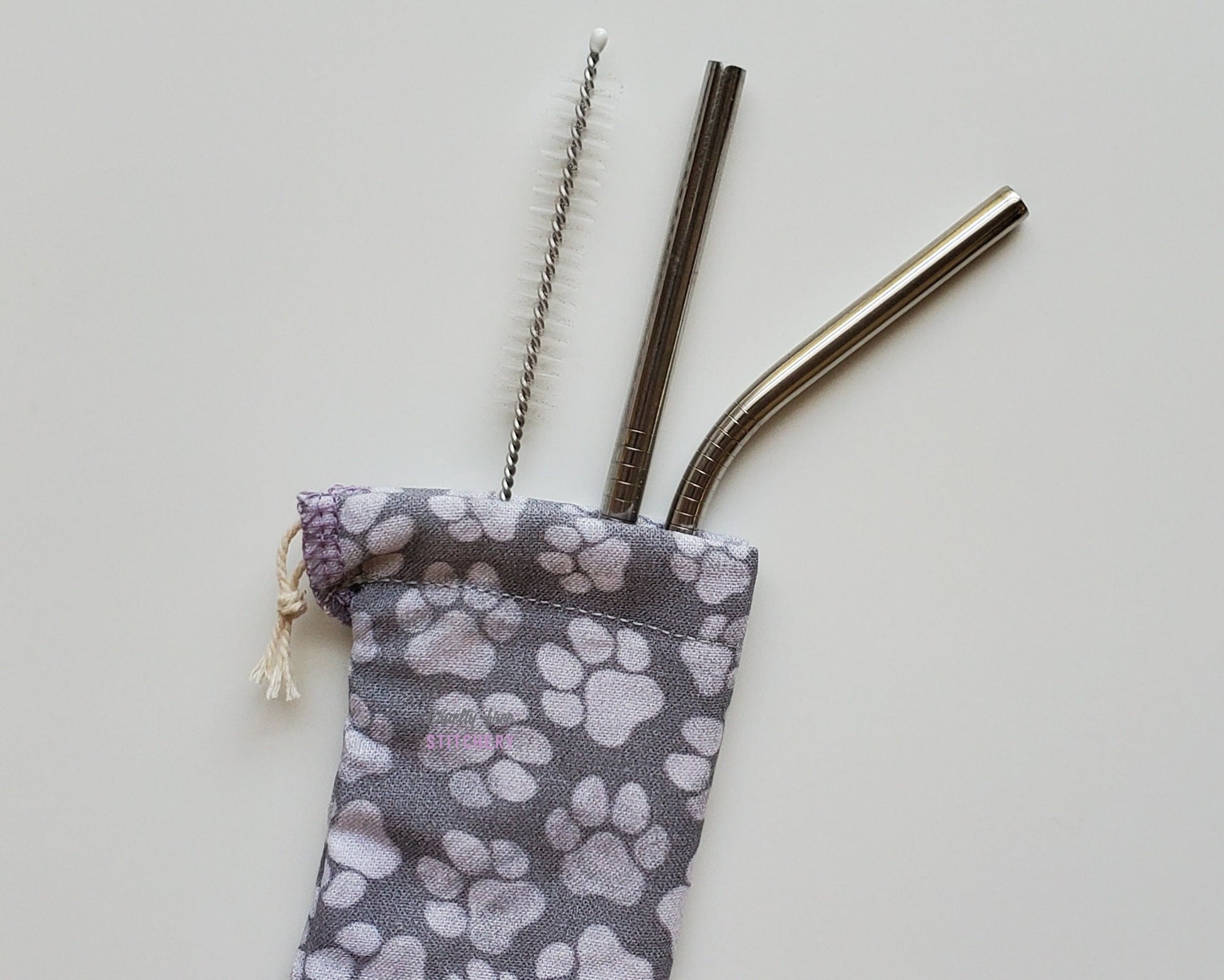 Reusable straw pouch with stainless steel straws sticking out the top. The fabric of the pouch is grey with various sizes of faded white paw prints, and it has a drawstring closure.