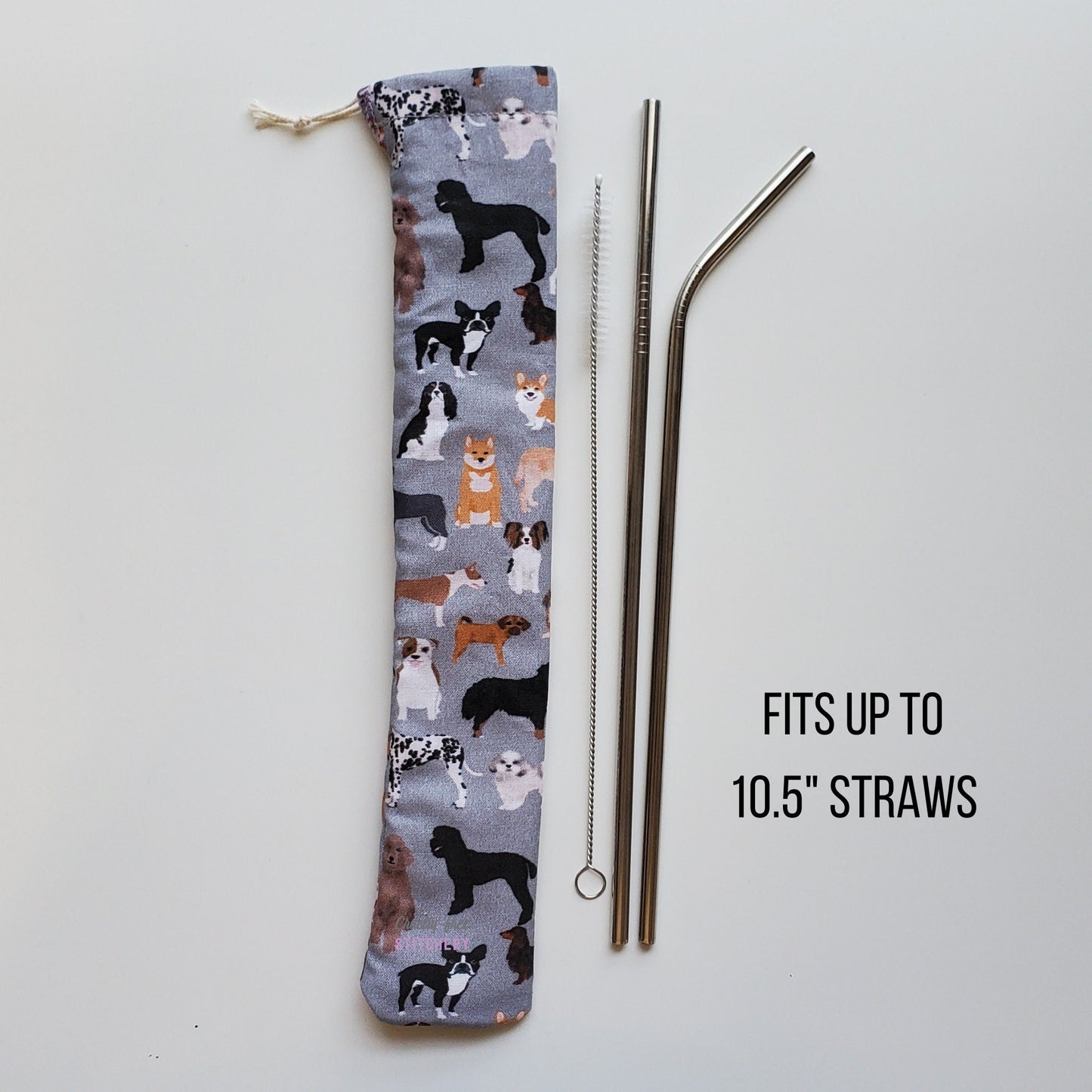Reusable straw pouch in the same dog print laying vertically next to a straw cleaner brush, a straight stainless steel straw, and a bent stainless steel straw. Text reads &quot;fits up to 10.5 inch straws&quot;