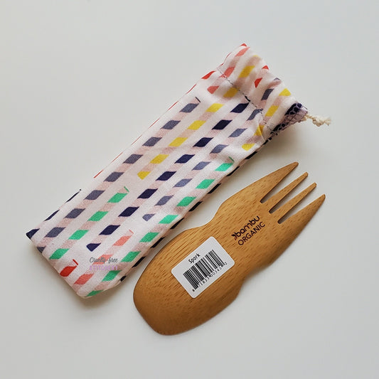 Reusable spork pouch laying diagonally next to an upside-down bamboo spork.