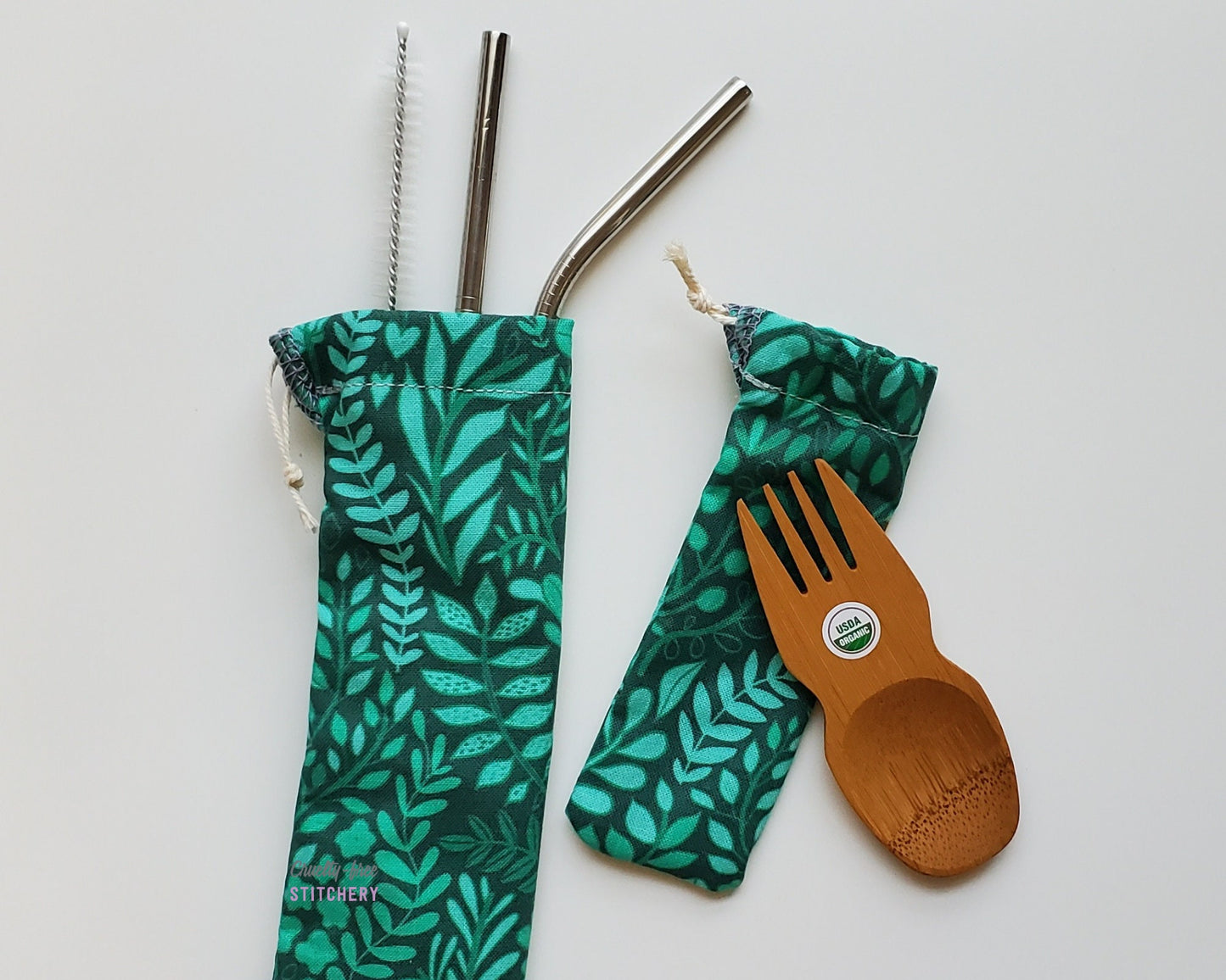 Reusable bamboo spork and straw pouch set. The pouches are both a dark green with lighter green leaves and vines.