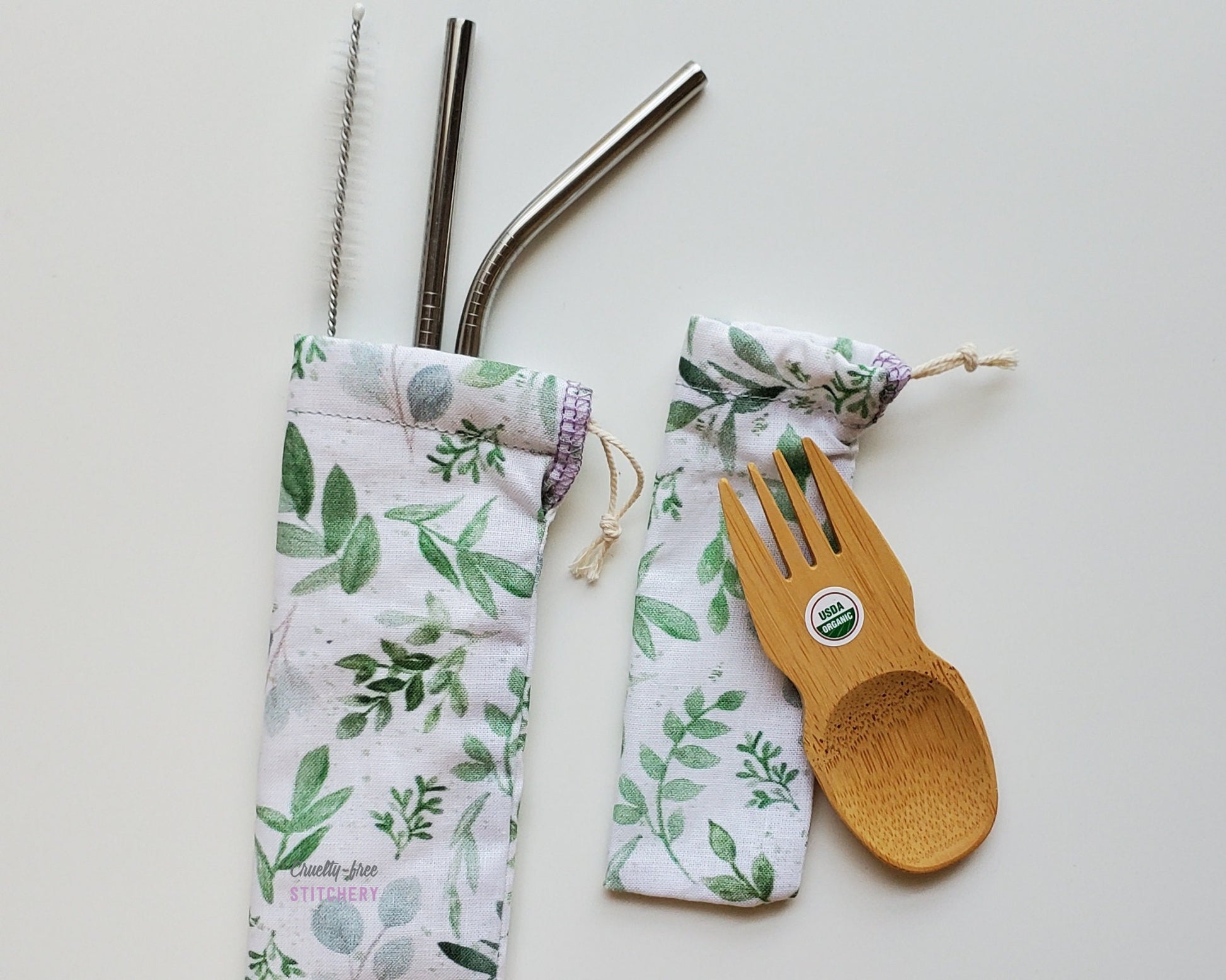 Reusable bamboo spork and straw pouch set. The pouches are both a white fabric with green eucalyptus leaves printed on.