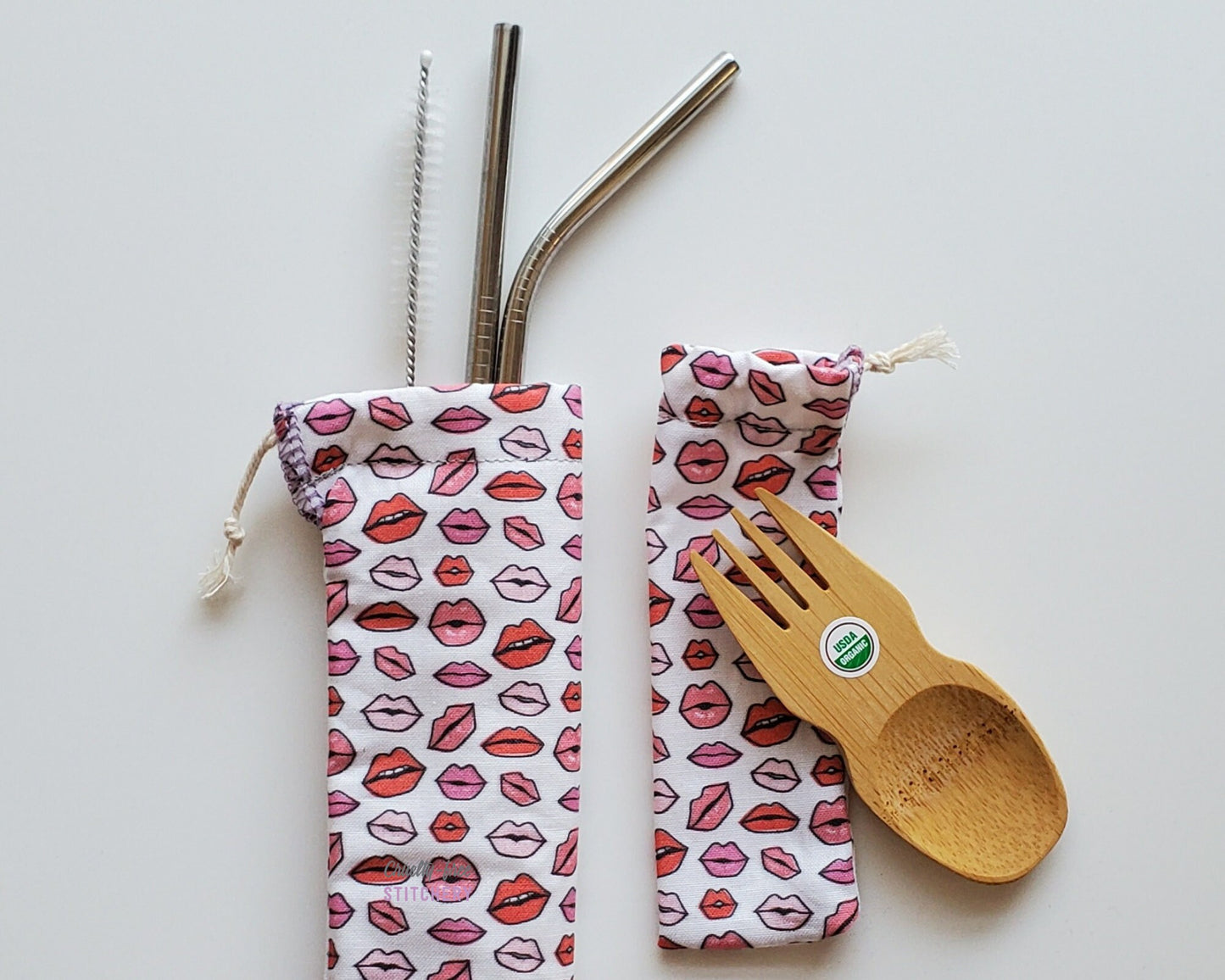 Reusable bamboo spork and stainless steel straw pouch set. The pouches are both white with tiny lips in varying shades of pink.