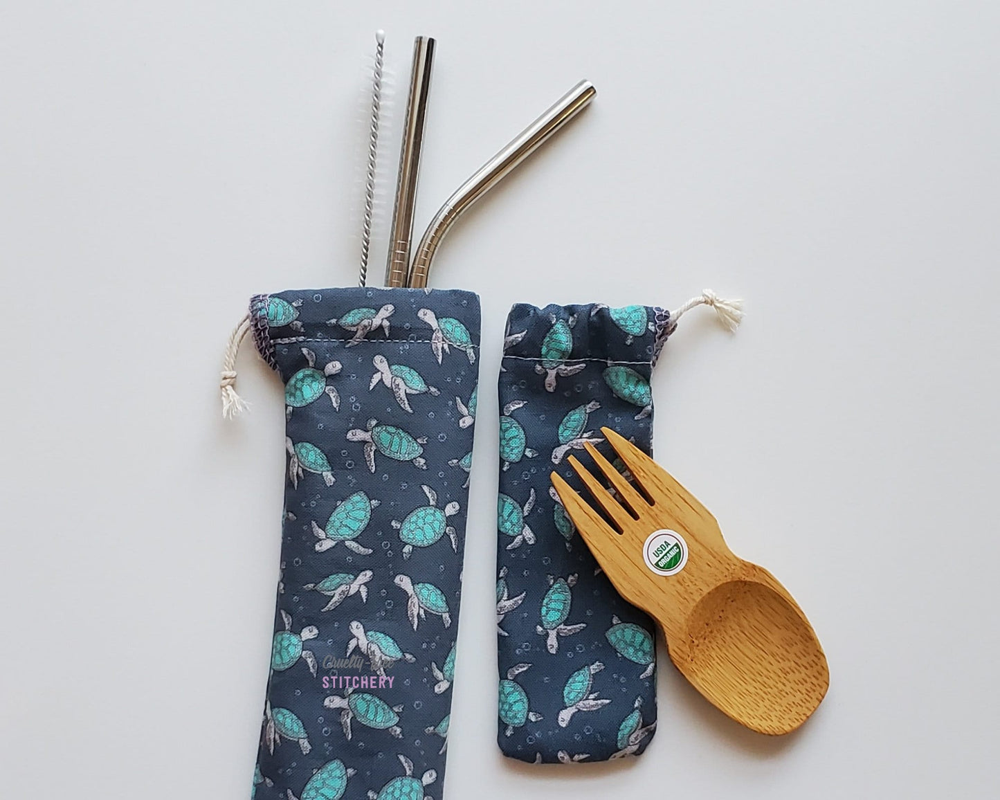 Reusable bamboo spork and stainless steel straw pouch set. The pouches are both dark navy blue with tiny sea turtles printed on the fabric.