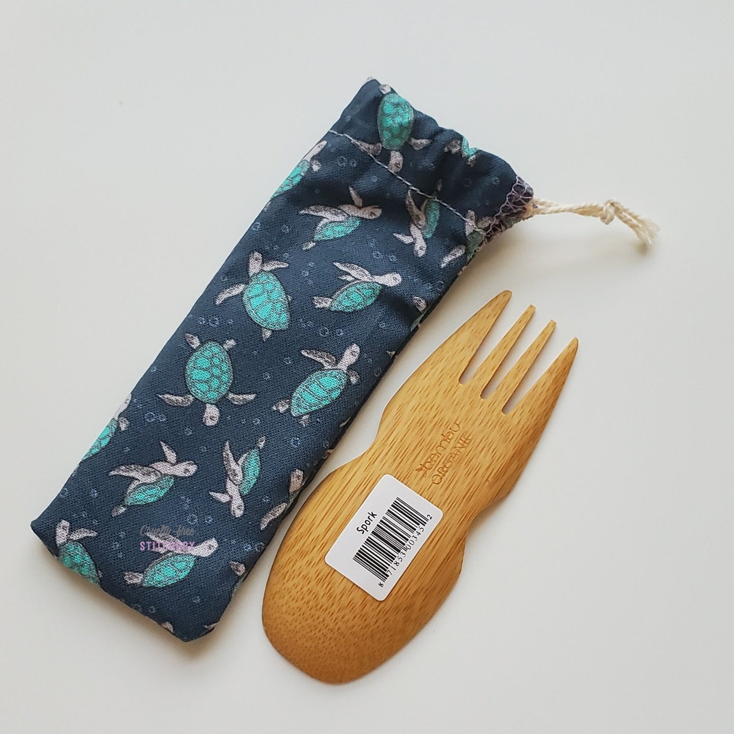 Reusable spork pouch laying diagonally next to an upside-down bamboo spork.