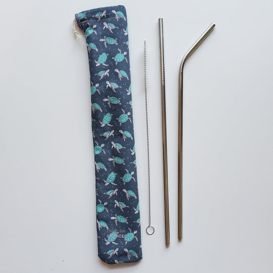 Reusable straw pouch in the same sea turtle print laying vertically next to a straw cleaner brush, a straight stainless steel straw, and a bent stainless steel straw.