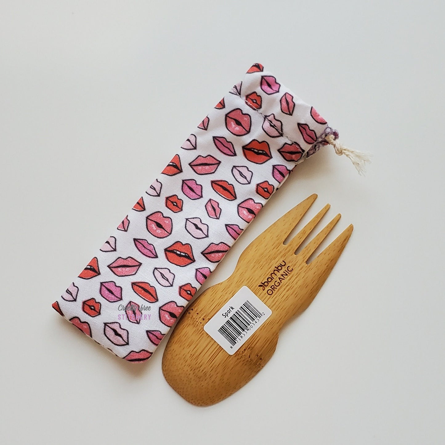 Reusable spork pouch laying diagonally next to an upside-down bamboo spork.