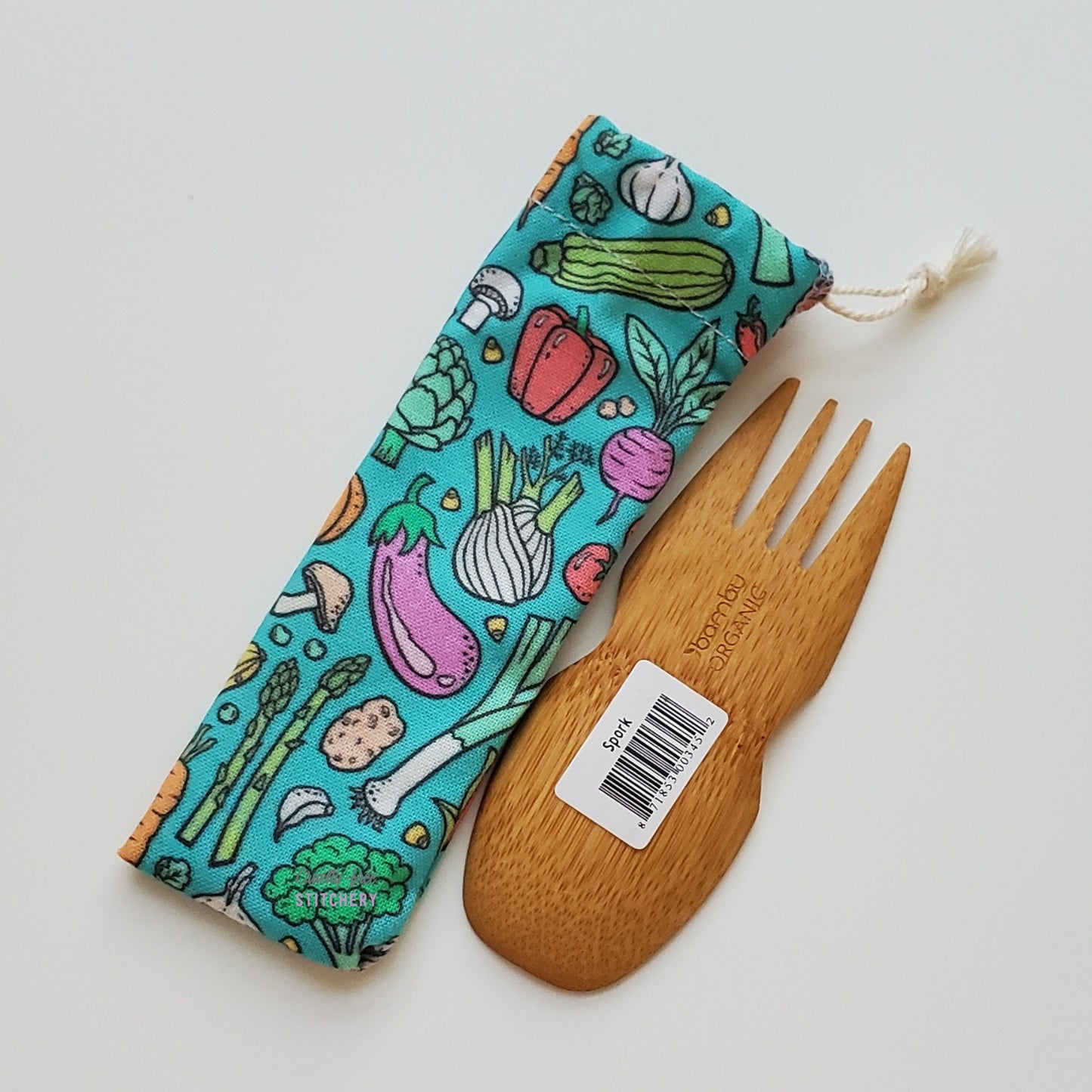 Reusable spork pouch laying diagonally next to an upside-down bamboo spork.