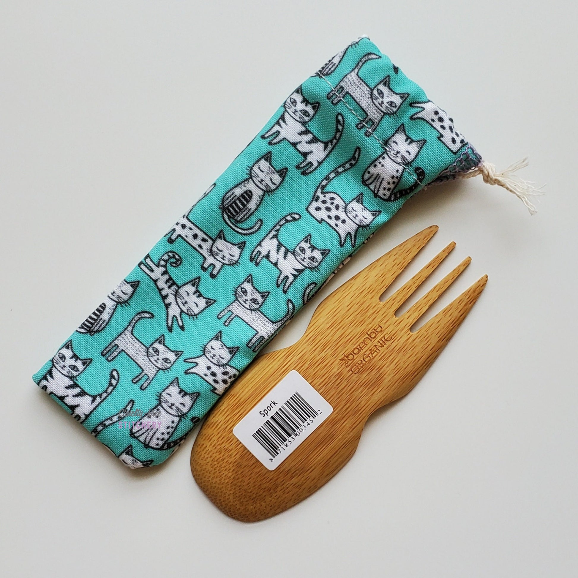 Reusable spork pouch laying diagonally next to an upside-down bamboo spork.