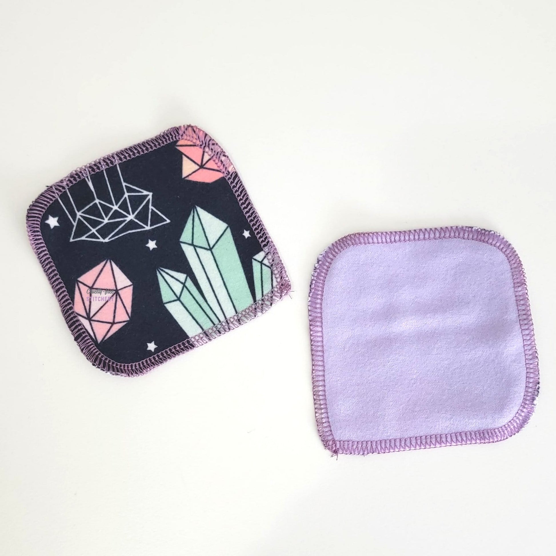 Two reusable cotton rounds, one face-up showing the crystals print, and one face-down showing the solid light purple on the back.