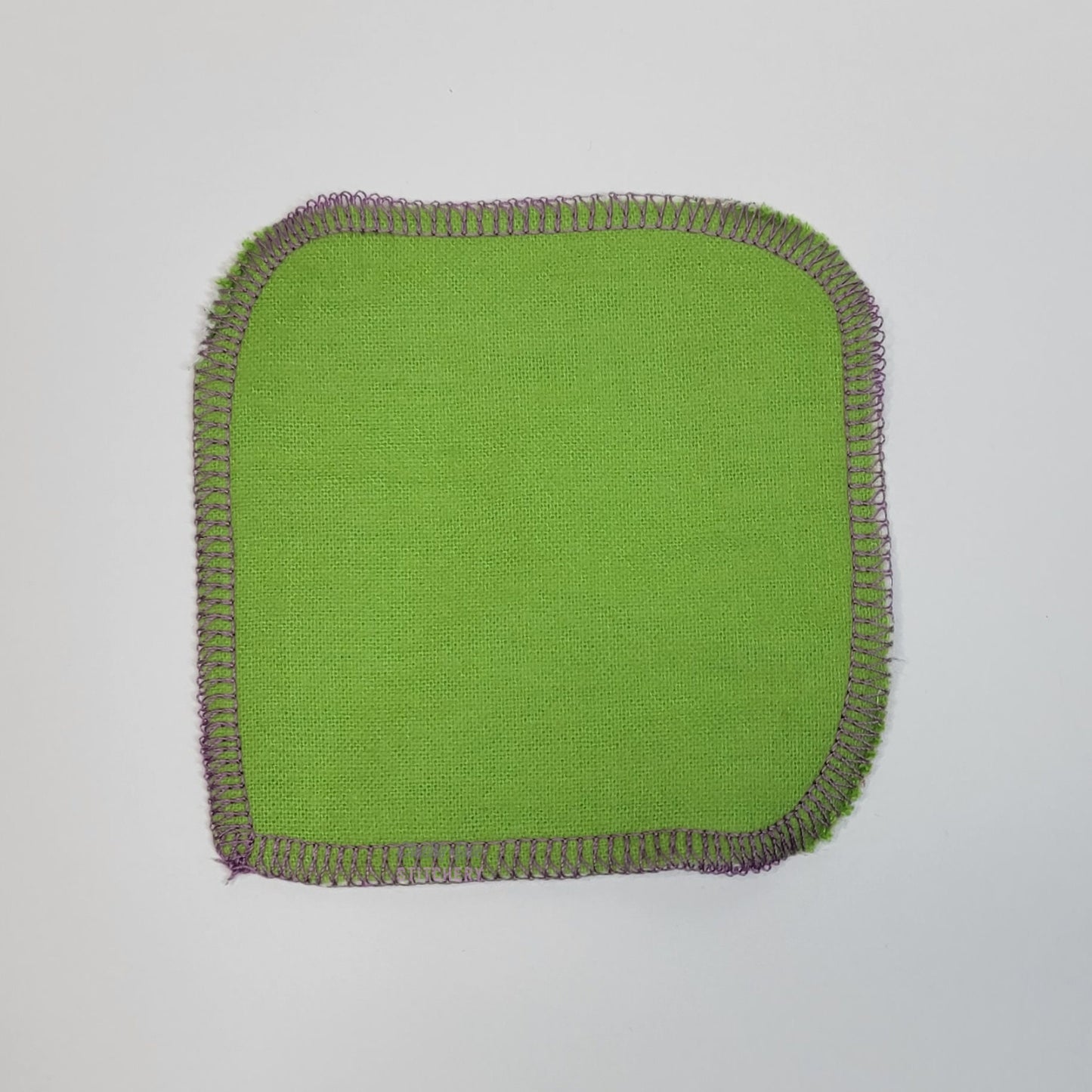 The back of one reusable cotton round, a solid light green.