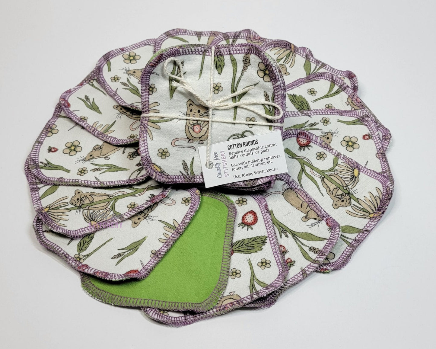 Mouse print reusable cotton rounds, arranged in a circle with a bundled pack in the center. They are a rounded square shape, and stitched together with light purple thread.