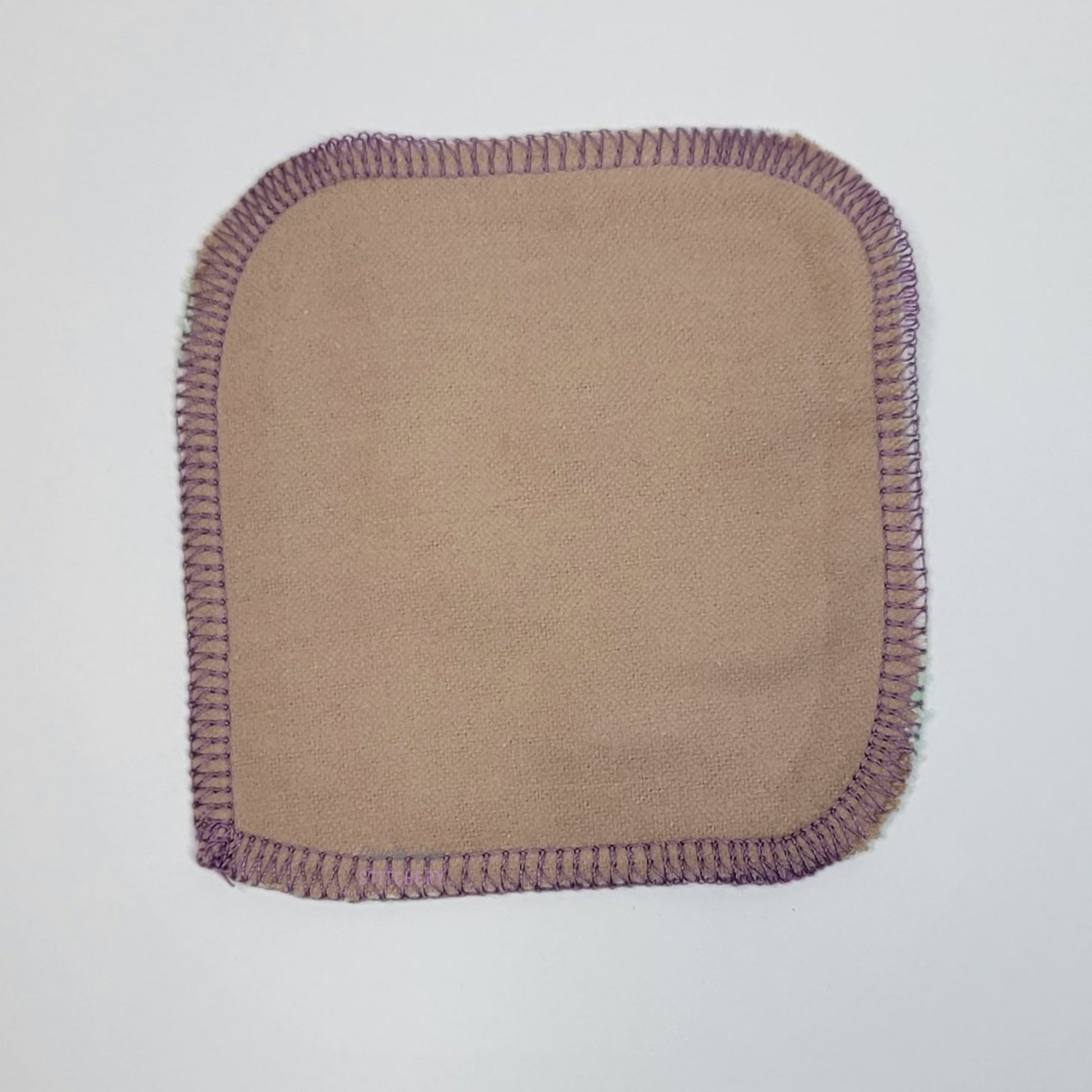 The back of a goats print reusable cotton round, it is a solid light tan color.