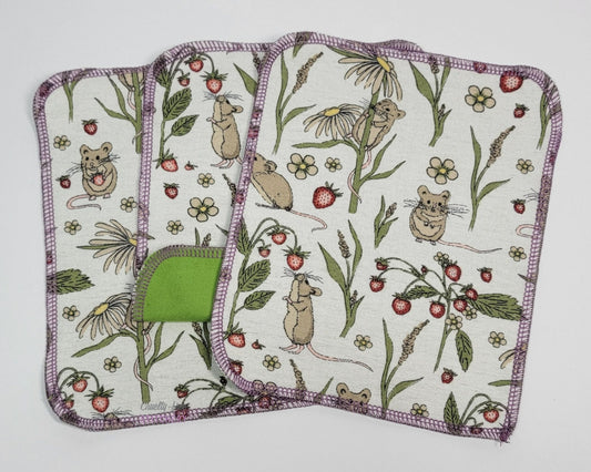 Mouse print reusable cloth wipes. Three wipes laid out, with the center one folded back to show that the back side is a light green. They are an off-white with tan mice, dandelions, and strawberry plants.