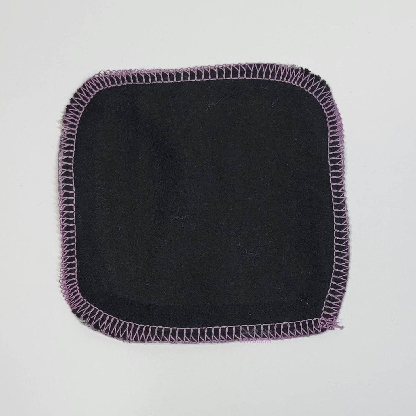 The back of one reusable cotton round - showing the back which is solid black.